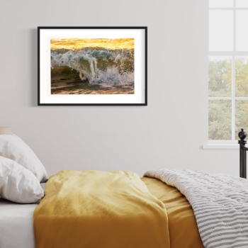 Framed photographic print in a bedroom of a closeup of an ocean wave breaking at sunrise with warm yellow colors by Jason Alders